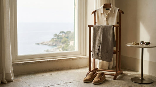 Folded knit polo and taupe trousers on a wooden valet chair with loafers by a bright window