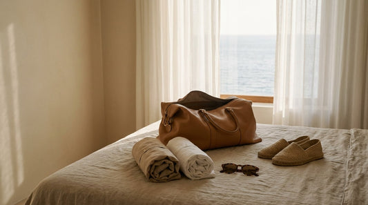 Open tan leather weekender bag with neatly rolled linen on a sunlit Mediterranean villa bed